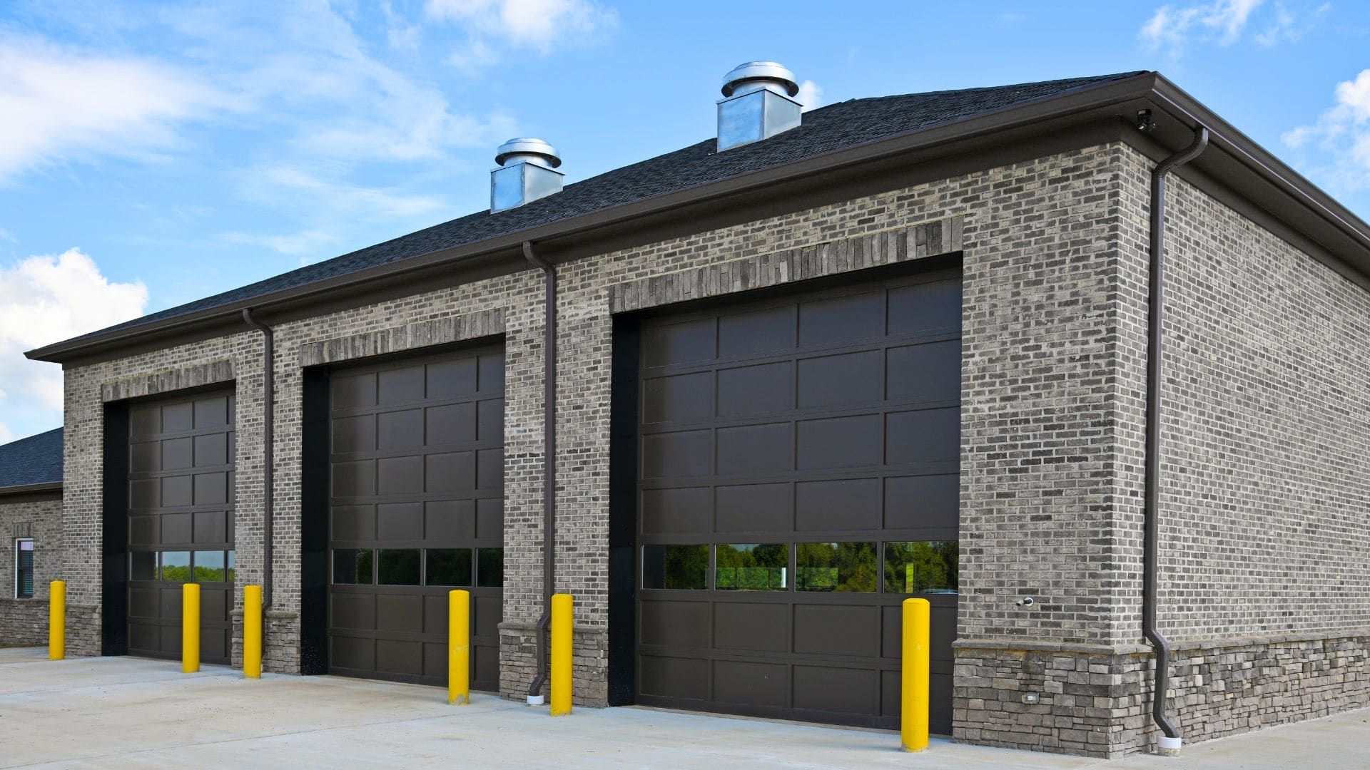 Commercial building with three brown overhead doors and safety bollards