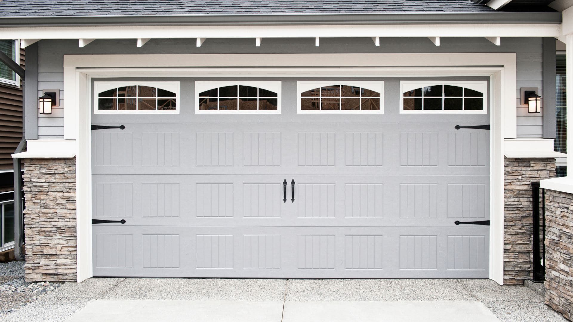 Grey carriage-style garage door with windows and decorative hardware