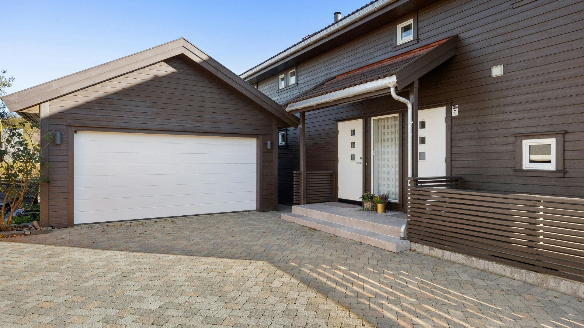 Modern dark-clad home with a white flush-panel double garage door